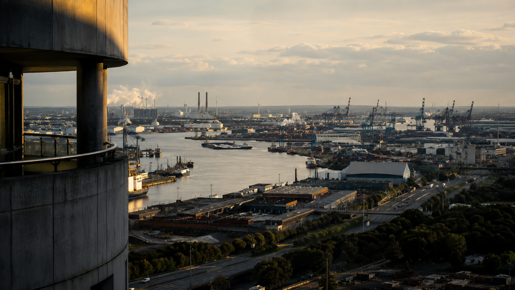 A working river port seen from a high vantage point at dusk, container cranes, warehouses and a highway running to the horizon